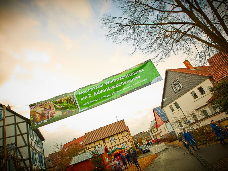 Das Banner zum Neuentaler Weihnachtsmarkt hängt über einer Straße, auf der Menschen laufen und ein Marktstand steht.