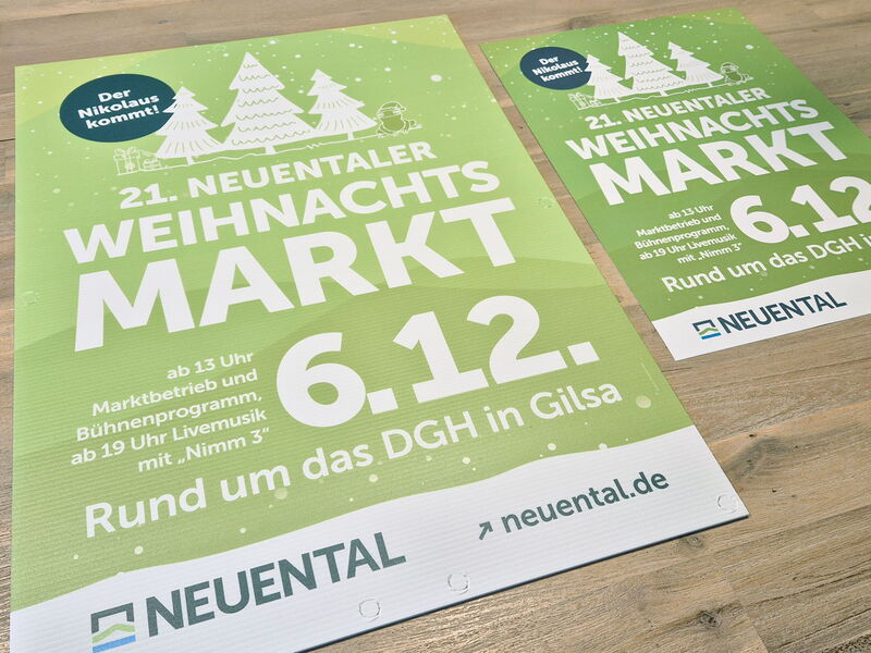 Zwei Plakate zum Weihnachtsmarkt der Gemeinde Neuental in verschiedenen Größen liegen auf einem Holztisch