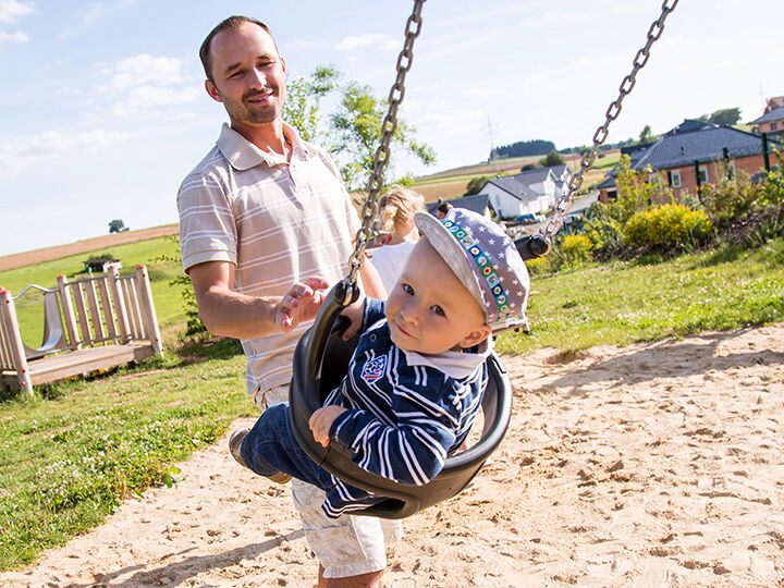 Ein Vater schubst sein Kind in einer Schaukel auf einem Spielplatz der Stadt Frankenberg an