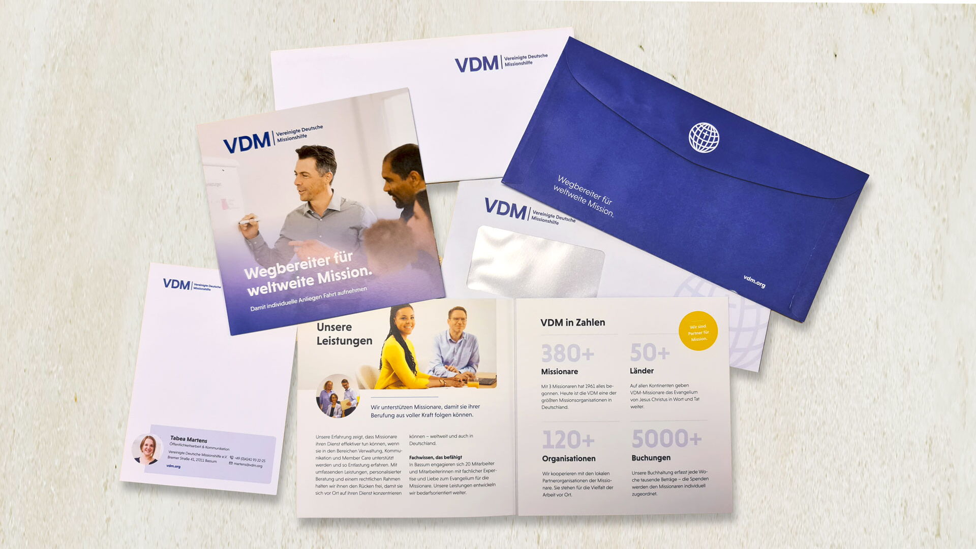 Briefumschläge der VDM und Broschüren mit Infos über die VDM liegen verteilt auf einem beigen Hintergrund