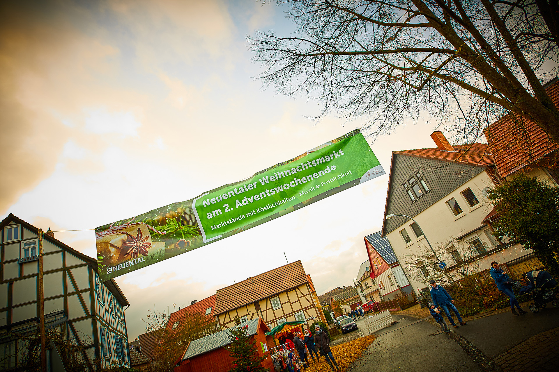 Das Banner zum Neuentaler Weihnachtsmarkt hängt über einer Straße, auf der Menschen laufen und ein Marktstand steht.