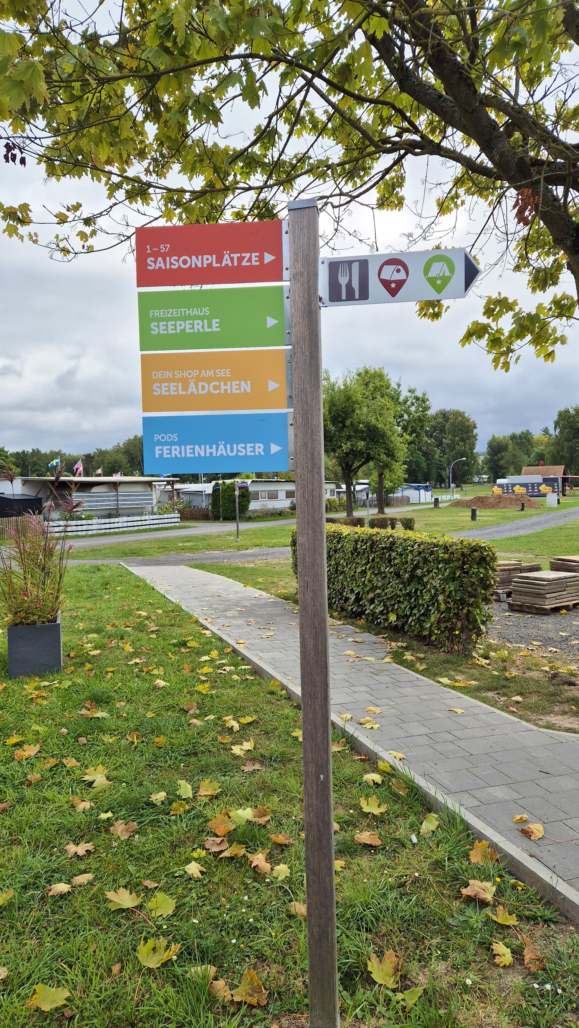 Ein Wegweiserschild auf einer Weise mit Weg zeigt mit verschiedenen Farben die Richtungen zu Saisonplätzen, dem Ferienhaus Seeperle, Seelädchen sowie den Ferienhäusern des Ferienparks Neuenhainer See.