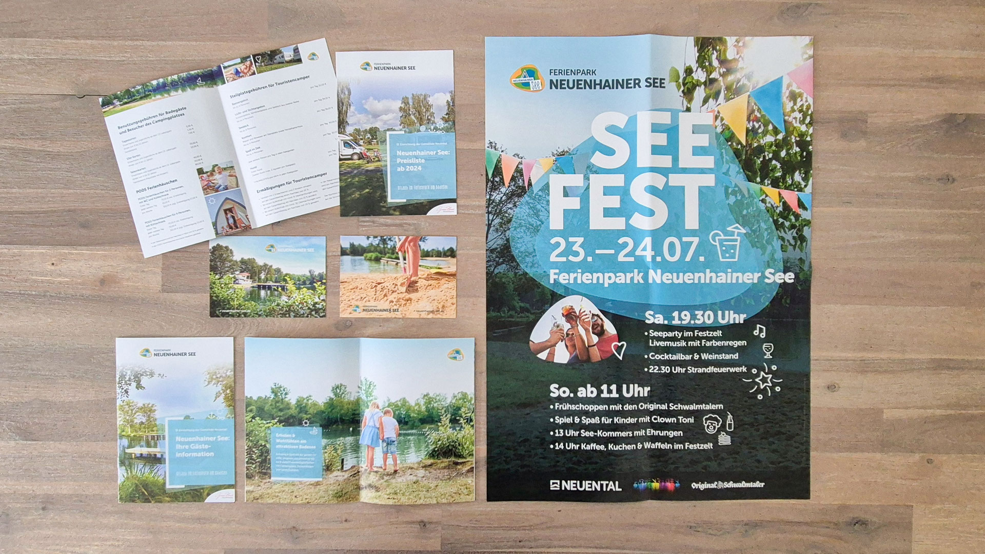 Auf einem Holztisch liegen die Broschüre, Postkarten, Preislisten und ein Plakat des Ferienparks Neuenhainer See.