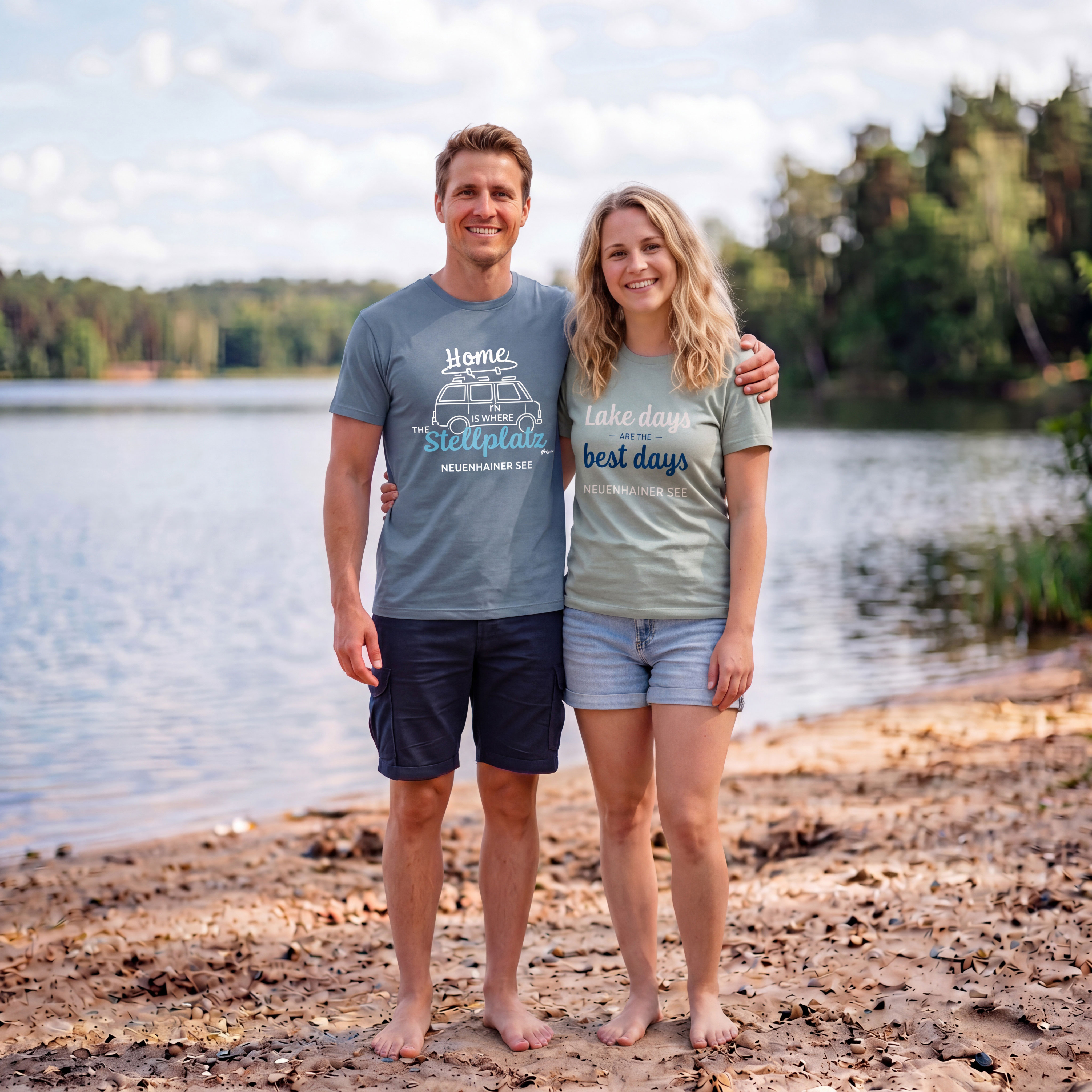 Mann und Frau stehen Arm in Arm am Strand an einem See und lachen in die Kamera.