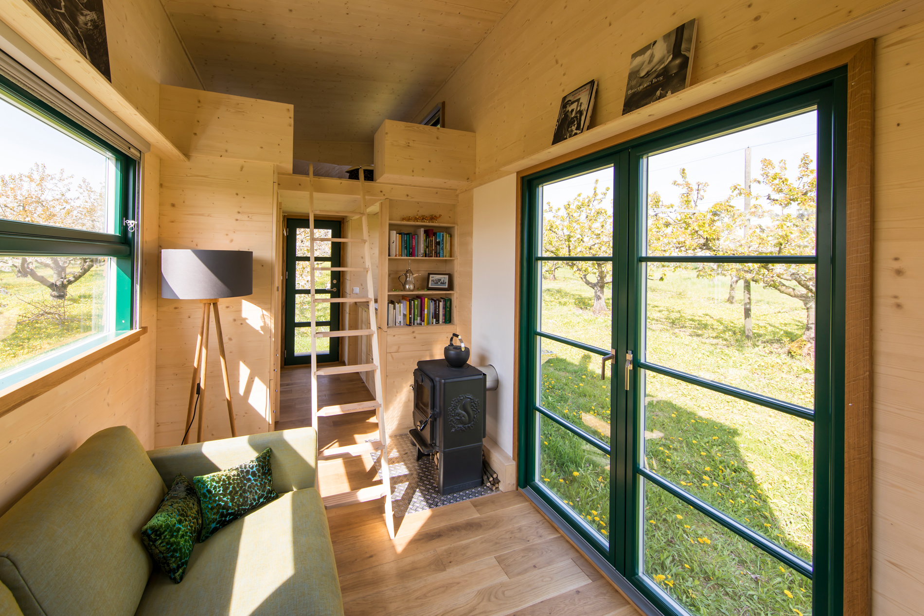 ein Tiny House der Tischlerei Bock wird von innen gezeigt mit einem Sofa, einem Ofen und einer Leiter, die hoch zum Bett führt