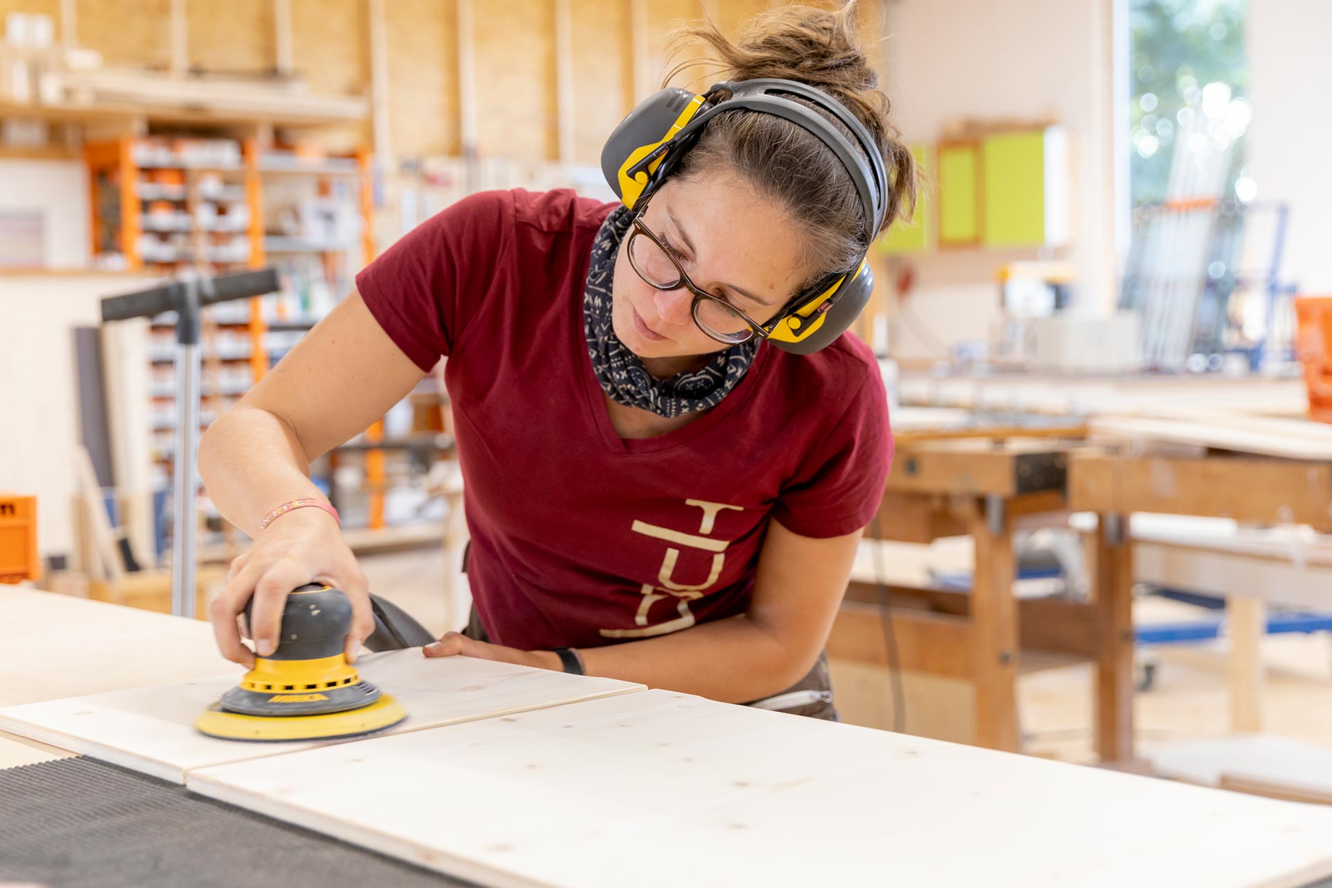 eine Schreinerin der Tischlerei Bock schleift Holz mit einer Maschine und trägt Ohrschützer